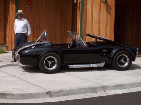1997 Ford Mustang - A black convertible sports car with side pipes and silver racing stripes is parked on a concrete surface.