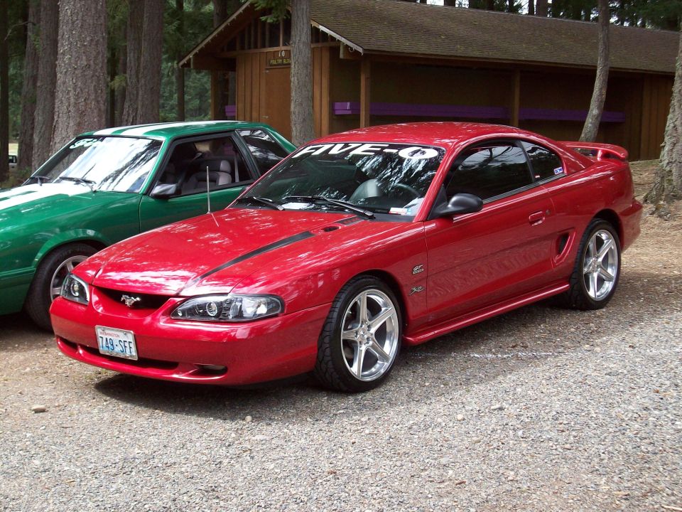 1997 Ford Mustang coupe with aftermarket wheels parked next to a green Mustang