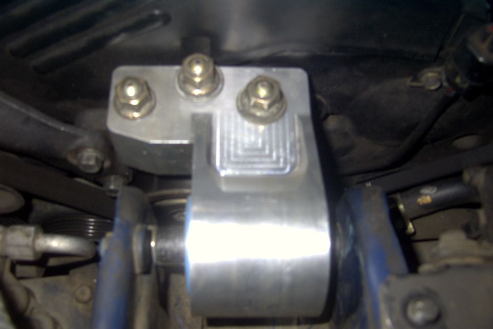 Close-up of an aftermarket aluminum motor mount with bolts and a ribbed texture
