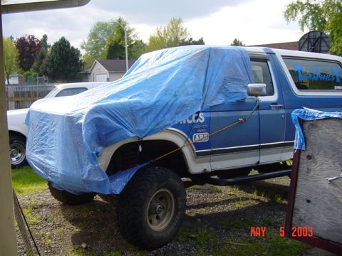 1989 Ford Bronco - 1989 Ford Bronco project vehicle partially covered by a tarp in a driveway.