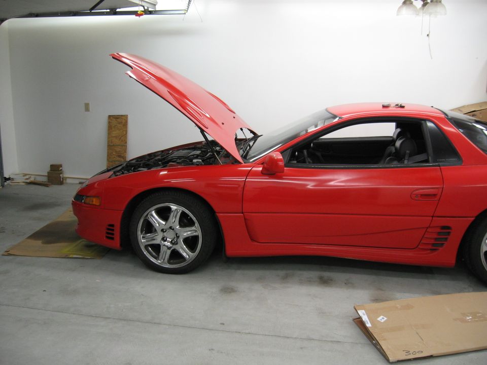 Red sports coupe with hood open, parked in a garage