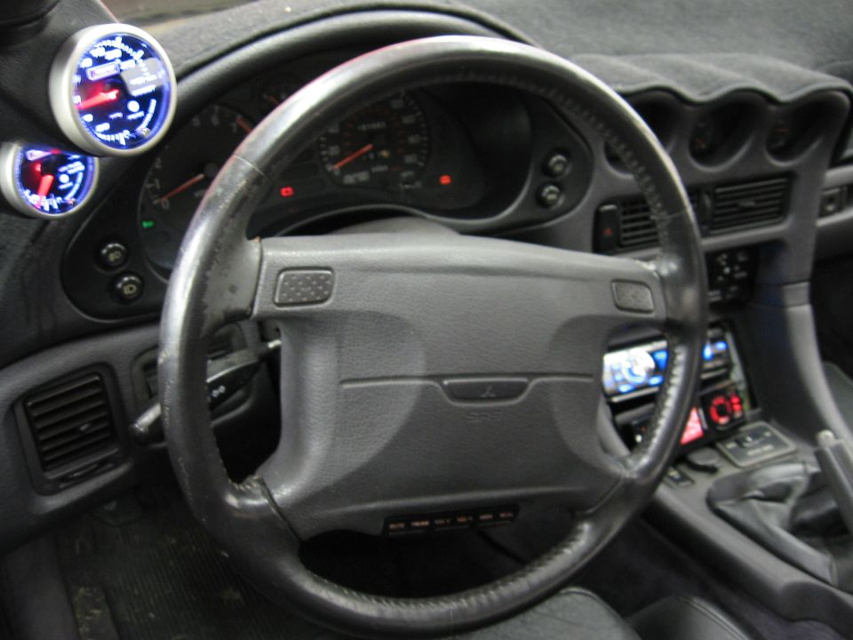 Interior of a 1991 Mitsubishi 3000GT showing steering wheel, dashboard, and aftermarket gauges
