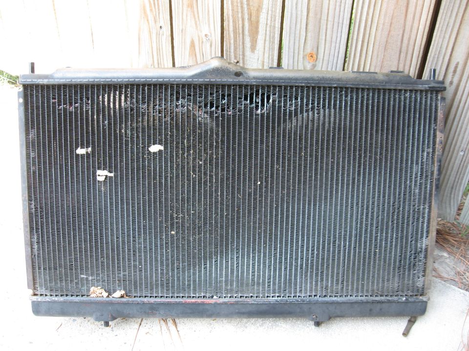 Black car radiator with damaged fins and debris, viewed from the front