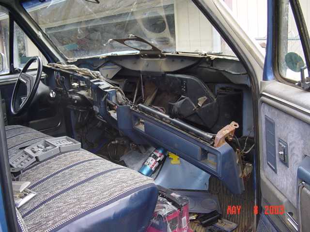 Blue truck interior with dashboard removed exposing wiring and ducts, striped bench seat