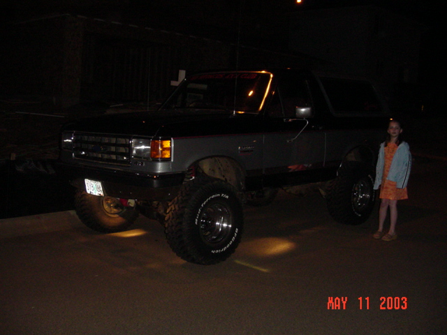 Lifted two-door SUV on large mud tires parked at night with a child standing beside it