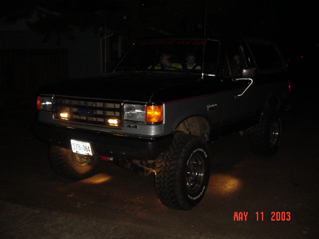Lifted Ford SUV with headlights on at night, kids visible inside the cab