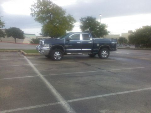 1995 Ford Bronco - Dark blue Dodge Ram pickup truck parked in a lot under a cloudy sky.