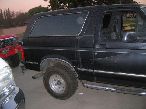 1985 Ford Bronco - Side view of a black SUV with chrome trim, side steps, and aftermarket wheels, parked next to another vehicle.