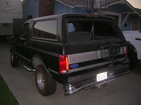 1985 Ford Bronco - The rear of a black Ford Bronco SUV is shown parked in a driveway with a house in the background.