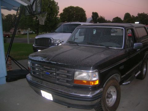 1985 Ford Bronco - A black Ford Bronco is parked in front of a white truck at dusk.