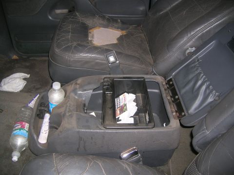 1985 Ford Bronco - The interior of the vehicle shows a worn driver's seat and a cluttered center console with trash and drinks.