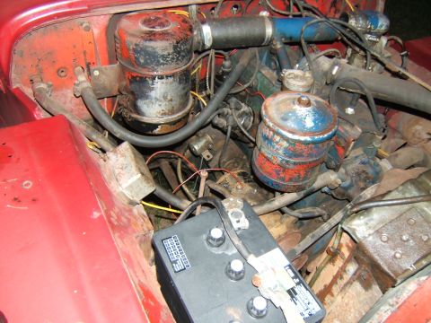 1946 Jeep CJ5 - The engine bay of a red Jeep, dual air cleaners and a prominent battery. Year is not discernible from this view.