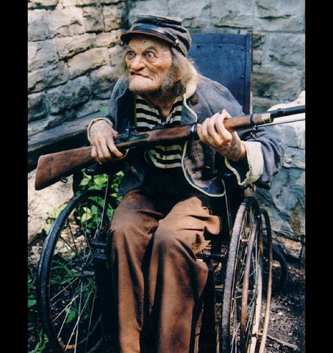 1971 Ford Ranchero - A weathered man in a cap and striped shirt holds a rifle while seated in a wheelchair.