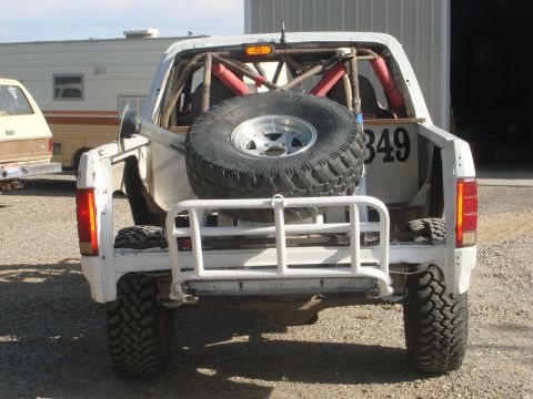 1990 Ford Bronco - Rear view of a white off-road race truck with an exposed roll cage, mounted spare tire and the number 349.