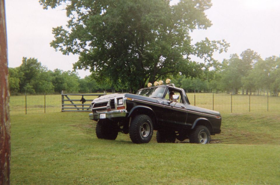 Black 1978 Ford Bronco with off-road tires and roof lights parked on a grassy field