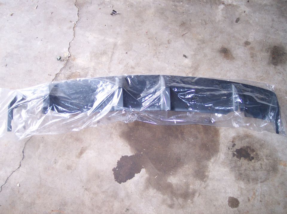 Black car bumper part wrapped in plastic, lying on concrete floor