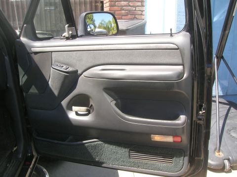 1985 Ford Bronco - Close-up of a vehicle's interior door panel, showing the armrest, door handle, and window controls.