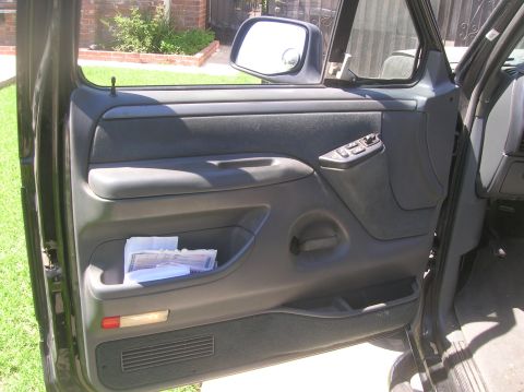 1985 Ford Bronco - Interior view of a car door panel with papers in the storage pocket.