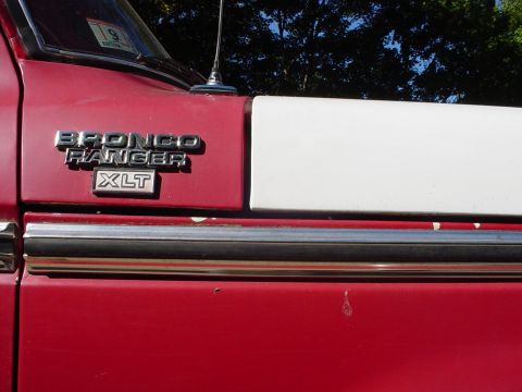 1978 Ford Bronco - The side of a red vehicle shows a "Bronco Ranger XLT" emblem, with a white stripe above it.