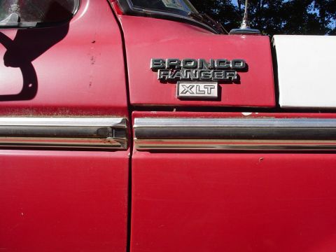 1978 Ford Bronco - Close-up of the side of a red 1978 Ford Bronco Ranger XLT, showing the emblem and chrome trim.