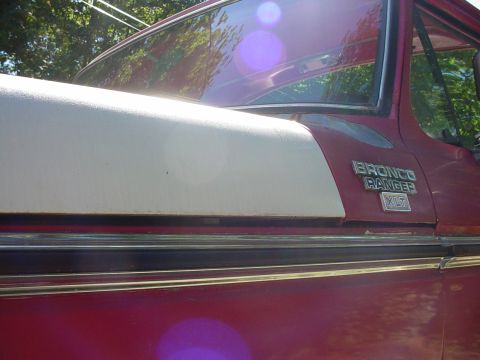 1978 Ford Bronco - Close-up side view of a red and cream 1978 Ford Bronco Ranger XLT, highlighting its distinctive fender badging.