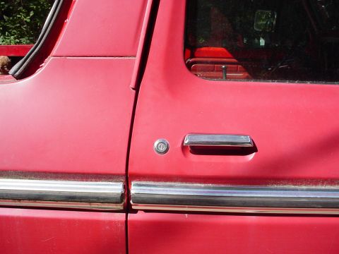 1978 Ford Bronco - Close-up of a red vehicle's side door, showing the chrome door handle and lock cylinder. The Supermotors.net watermark is present.