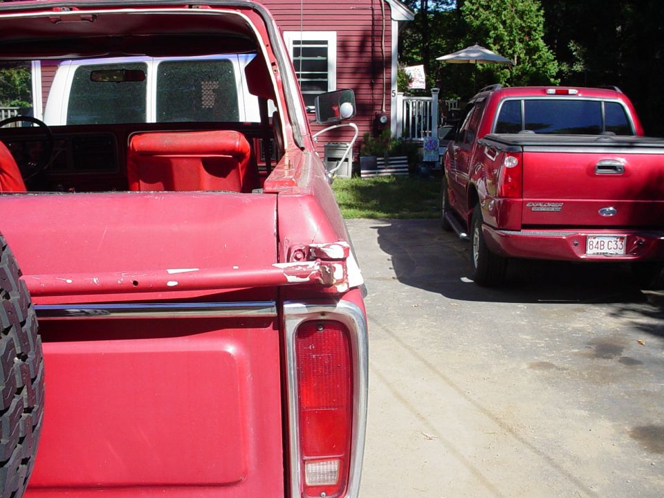 Red pickup truck rear with damaged taillight, parked next to a red SUV