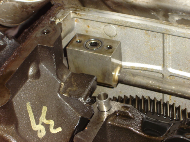 Close-up of engine block with some metal components and a gear visible. Yellow marking on block