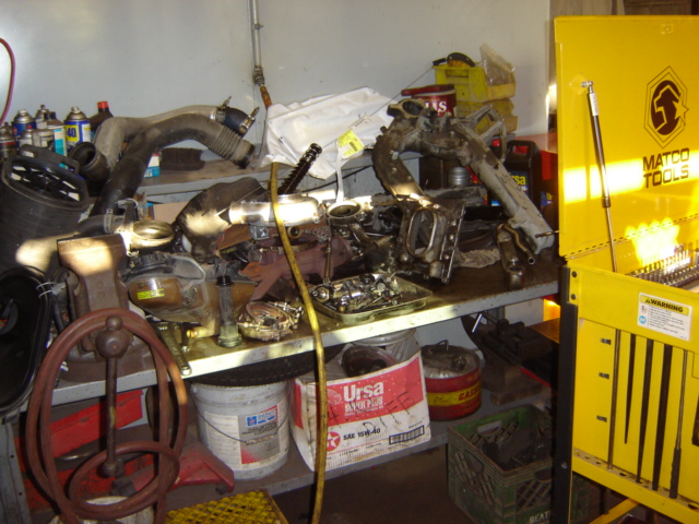 Workbench cluttered with engine parts, hoses, and a yellow Matco Tools toolbox