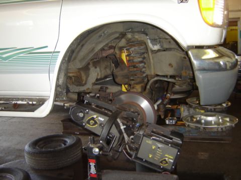 1992 Ford Bronco - A vehicle is undergoing brake and suspension work in a garage setting, with specialized equipment attached to the wheel assembly.