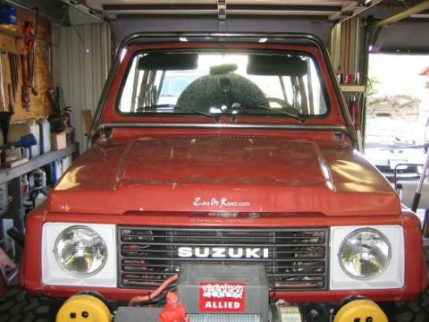 1987 Suzuki Samurai - Front view of a red 1987 Suzuki Samurai with an aftermarket exo cage and winch installed.