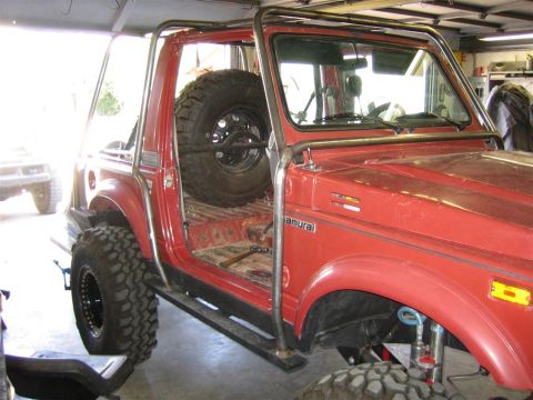 1987 Suzuki Samurai - This red SUV has a custom roll cage and is equipped with off-road tires and a spare tire inside.