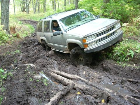 2000 Chevrolet Tahoe - A silver Chevrolet SUV navigates a challenging muddy terrain in a forest.