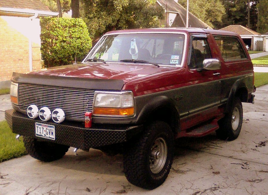 Dark red and gray Ford Bronco with billet grille, three round lights on black bumper, parked in driveway