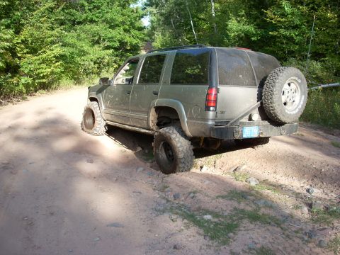 2000 Chevrolet Tahoe - This modified SUV, likely a late 1990s model, navigates a rough dirt path with its oversized tires and rear-mounted spare.