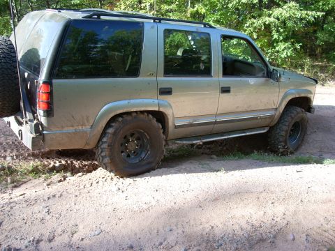 2000 Chevrolet Tahoe - Gold Chevrolet Tahoe with spare tire on rear bumper navigates a dirt path.