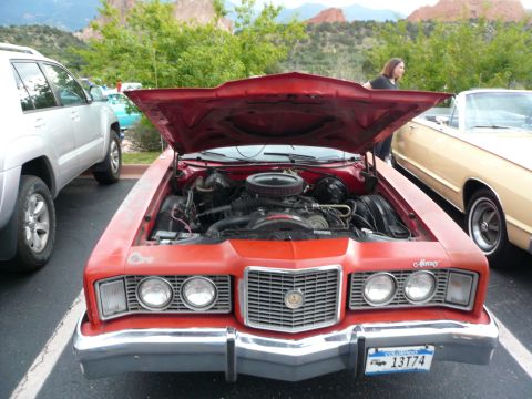 1975 Ford Ranchero - The front of a red 1975 Ford Ranchero is visible with its hood open, revealing the engine bay.