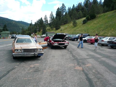 1975 Ford Ranchero - Several vehicles are parked in a lot, including a 1975 Ford Ranchero with its hood open.