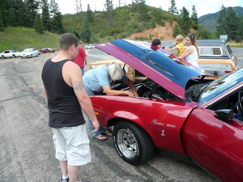 1975 Ford Ranchero - People gather around a red 1975 Ford Ranchero with its hood up, possibly discussing engine work.
