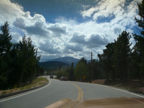 1975 Ford Ranchero - A scenic drive on a mountain road with two vehicles ahead, under a dramatic sky.