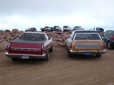 1975 Ford Ranchero - Two classic vehicles are parked on a rocky, dusty surface with other cars in the background.
