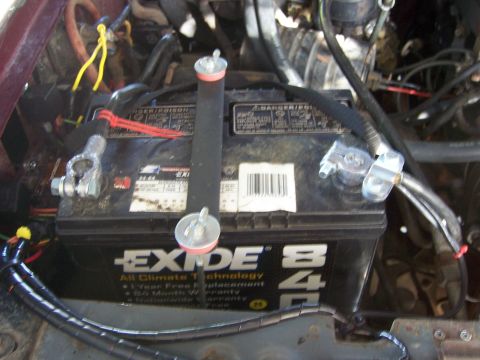 1991 Ford Bronco - Close-up of a battery hold down strap securing an Exide battery within an engine compartment.