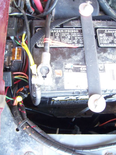 1991 Ford Bronco - Close-up of a car battery and its associated wiring and hold-down strap.