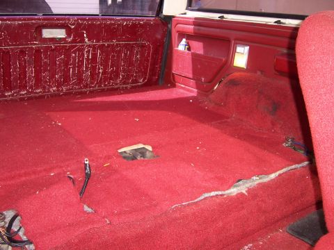 1991 Ford Bronco - The interior of the vehicle shows red carpeting and worn red door panels with visible damage.