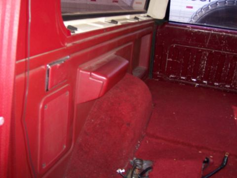 1991 Ford Bronco - The interior of a vehicle features red carpeting and side panels, with a spare tire visible in the background.