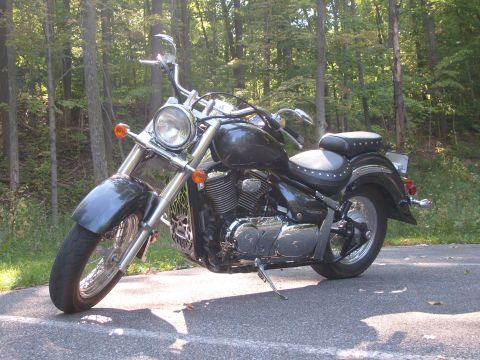 1993 Ford Bronco - A dark cruiser motorcycle is parked on a paved surface with a wooded area behind it.