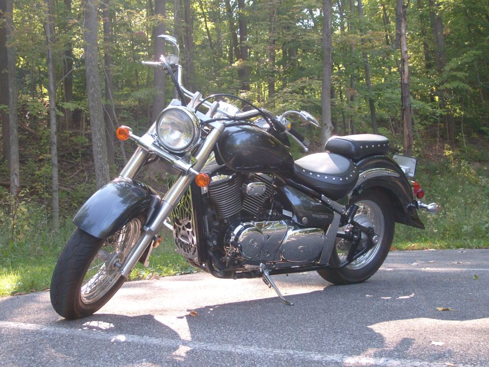 black cruiser motorcycle parked on asphalt road, trees in background