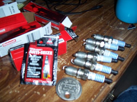2003 Ford Ranger - Several spark plugs and a packet of anti-seize compound are laid out on a wooden surface.