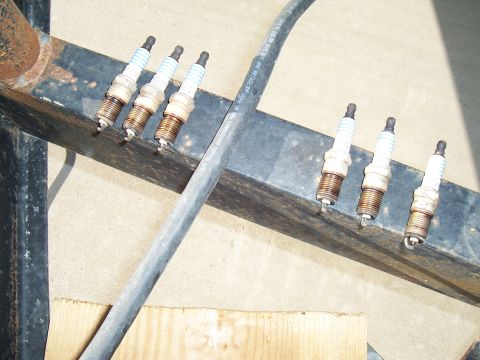 2003 Ford Ranger - Six spark plugs are laid out on a metal bar, with a thick black cable running diagonally across the frame.