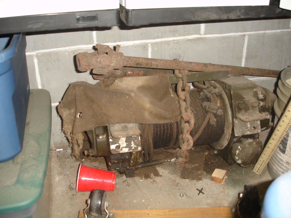 Old winch with chain and cover, sitting on a concrete floor next to a blue bin
